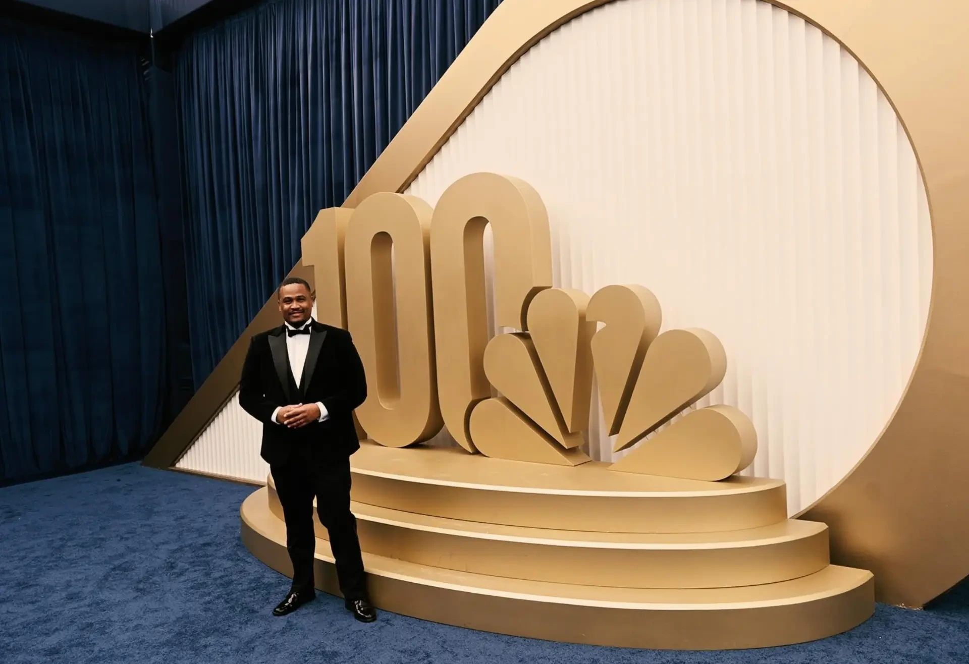 E'Ian West in a tuxedo beside the NBC 100 Years display